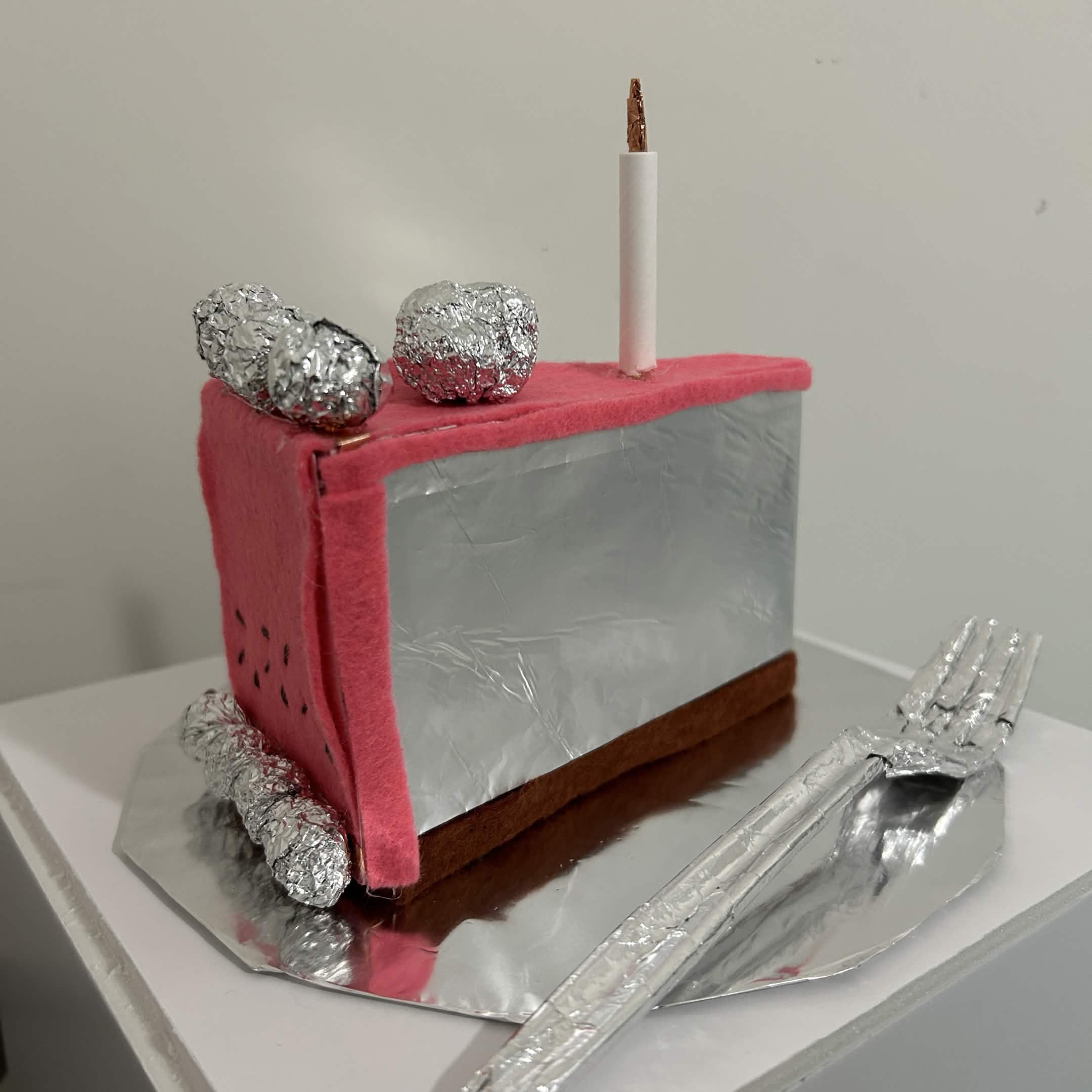 A cake slice made out of different materials. Mainly using aluminum foil for conductivity. Other materials used are card stock, copper tape, scotch tape, 12 gauge wire, soda cans, craft felt, and a plastic fork. Non conductive materials were used to block circuits from touching each other. <div class='container'> <iframe class='responsive-iframe' src='https://yago.phoenix.sheridanc.on.ca/Module%203%20Cake/'  width=100% height=500px></iframe></div>